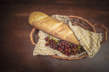 wicker basket with loaf of bread and red grapes on wooden background