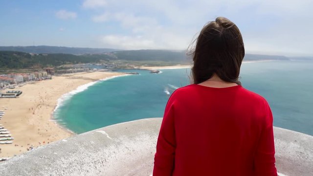 Woman in red dress enjoys a view of the ocean coast near Nazare, Portugal. Slow motion