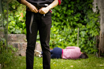 Close up of a man adjusting his pants after a sexual abuse, with woman laying in the ground behind the rapist. Rape and Sexual abuse concept