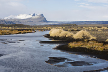 Autumn landscape in Iceland with a river, black sand and dry grass in foreground