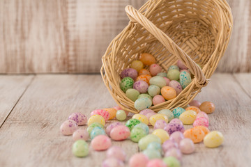 Fototapeta na wymiar Pastel Colored Easter Egg Candy Spilling Out of Wicker Basket on Wood Background