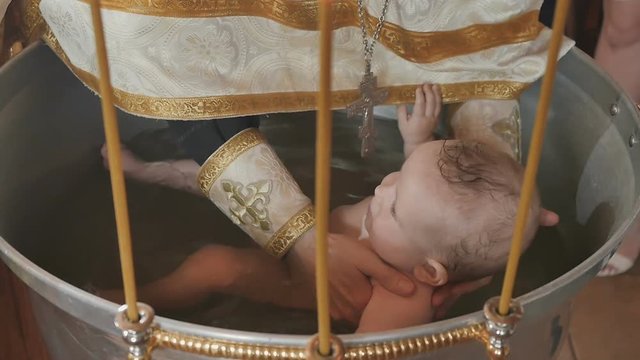 The priest dipped a baby in water in font during ritual of baptism