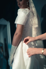 Vintage 1940s bride looking over shoulder at seamstress finishing dress.