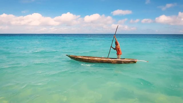 Aerial view of a poor fisherman with a torn shirt sails on a small boat on clear blue water along a tropical beach with beautiful hotels in Africa. Indian Ocean. Zanzibar. 2017