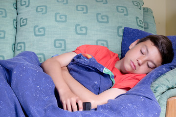 Unwell young teenage boy wrapped in a duvet on a sofa