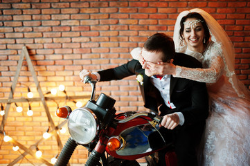 Fototapeta na wymiar Amazing wedding couple posing with a huge old motorcycle in a room full of lights.