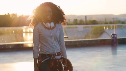 Young beautiful african woman walking on the rooftop on the city background during sunset. - Powered by Adobe