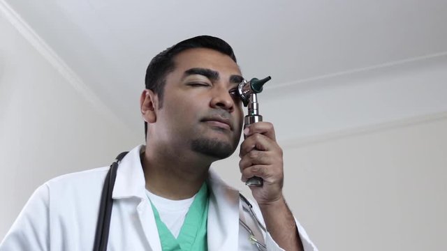 Young attractive doctor looking through otoscope 
