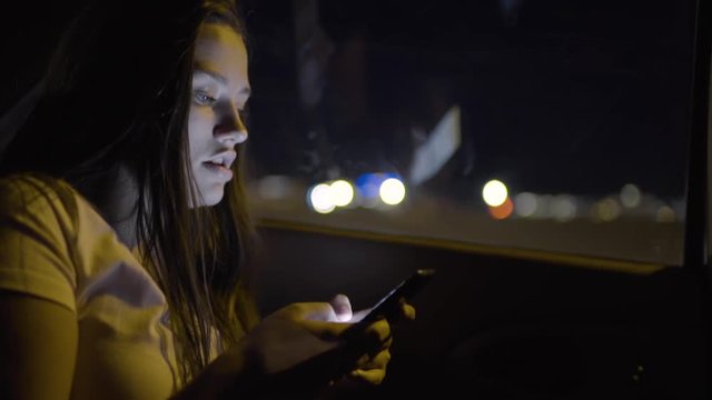 Slow Motion Closeup Of Teen Girl, Sits In Back Seat Of Moving Car On Freeway, She Checks Her Smartphone And Looks Out Window