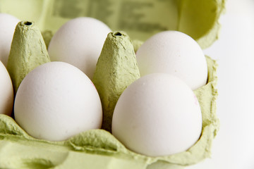 Six white eggs in a open green package, viewed from the top, against a white background closeup.