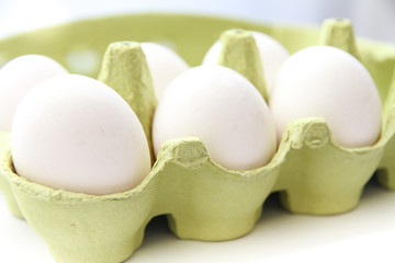 Six white eggs in a open green package, viewed from the top/side, against a white background closeup.