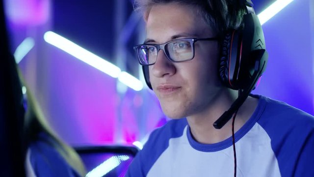 Teenage Boy Gamer Plays in Competitive Video Game on a eSports Tournament/ Internet Cafe. He Wears Glasses and Headphones and Speaks into Microphone. Shot on RED EPIC-W 8K Helium Cinema Camera.