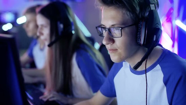 Professional  Boy Gamer Plays in Video Game on a eSports Tournament/ Internet Cafe. He Wears Glasses and Headphones and Speaks into Microphone. Shot on RED EPIC-W 8K Helium Cinema Camera.