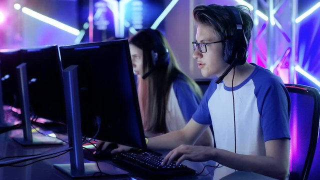 Team of Professional eSport Gamers Playing Video Games on a Cyber Games Tournament. Girls and Boys Have Headphones On, Arena is Lit with Neon Lights. Shot on RED EPIC-W 8K Helium Cinema Camera.