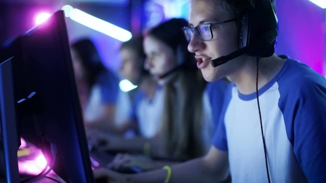 Depth of Field Shot of Team of Teenage Gamers Playing in Multiplayer PC Video Game on a eSport Tournament. They Speak in Microphones. Emotional Gaming Moment. 