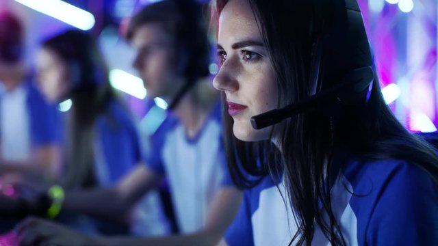 Beautiful Professional Gamer Girl and Her Team Participate in eSport Cyber Games Tournament. She Has Her Headphones and as a Team Leader She Commands Strategical Maneuvers into Microphone. 