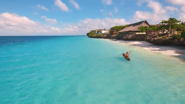 Aerial view of a poor fisherman with a torn shirt sails on a small boat on clear blue water along a tropical beach with beautiful hotels in Africa. Indian Ocean. Zanzibar. 2017