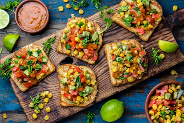Mexican Latin American style open sandwiches. Vegetarian toasts with maize, avocado, tomatoes on wooden board. Rustic wooden blue background. Top view
