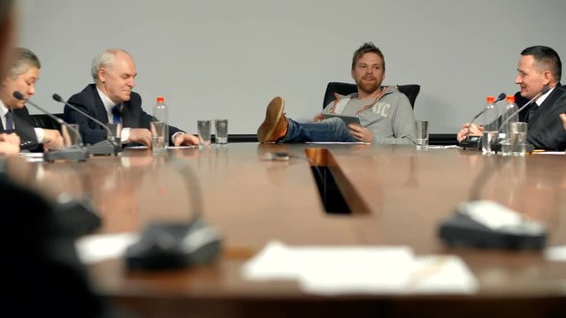 Young crazy CEO of the technology company heads the board of directors at his modern office. He behaves impressively, puts his feet on the table