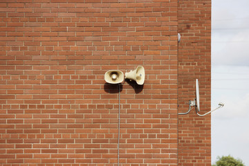 A brick wall of a residential building, two loudspeakers and a satellite dish against the sky