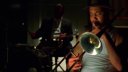 Trombone player in jazz band with drummer in the background.