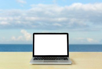 Fototapeta premium Laptop blank screen on table with sea and sky background