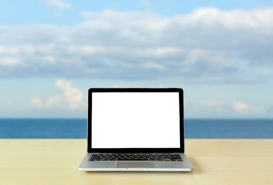 Laptop blank screen on table with sea and sky background © topzafoto