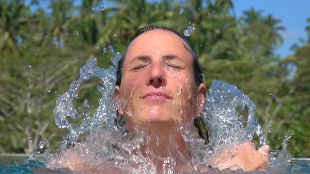 SLOW MOTION CLOSE UP: Portrait of pretty young girl on relaxing summer vacation in luxury jungle resort in sunny Bali. Woman splashing refreshing water on her face, waterdrops falling down her skin