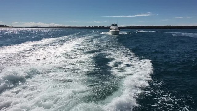 Motor boat cruising in the wake of a boat on a sunny day.