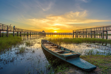 A beautiful golden sunset on the marsh. A row boat and a wooden bridge at the marsh at twilight. A...