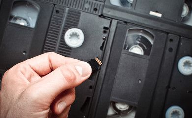 Micro sd memory card in hand on a background of video cassettes. Comparison of modern and retro...