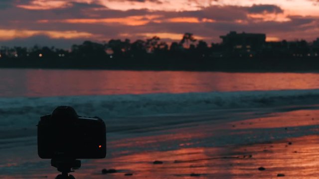 Camera shooting timelapse on the tripod on the beach in the sunset