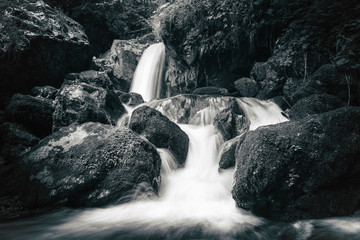 Panele Szklane Podświetlane  Widok na kamieniste bystrza w górskiej rzece. Szybki strumień wody przy długich czasach otwarcia migawki daje piękny efekt magii. Czarno-białe zdjęcie.