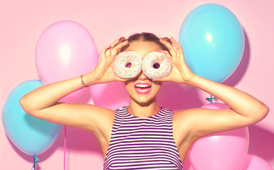 Joyful model beauty girl holding donuts and colorful air balloons over pink background