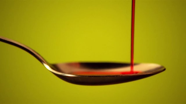 Red cough syrup type liquid pours onto a spoon.