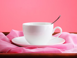 White cup on wooden table over pink