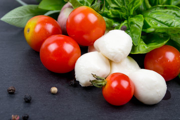 Mozzarella, cherry tomatoes and fresh basil, lemon, garlic. Ingredients for salad. On black slate stone chalkboard. Top view.