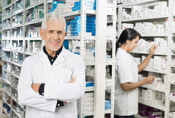 Obraz premium Senior Pharmacist Standing Arms Crossed While Colleague Checking
