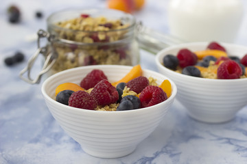 Bowls of  granola  with  fresh fruit on marble table.