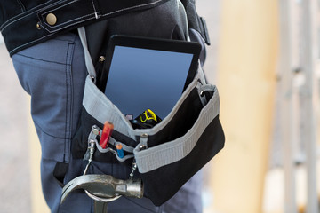 Midsection Of Carpenter With Tablet Computer And Tools In Bag