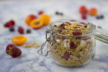 Bowls of  granola  with dry raspberries, cranberries and blueberries and fresh fruit on marble table.
