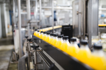Industrial factory indoors and machinery. Robotic factory line for processing and bottling of soda and orange juice bottles. Selective focus. Short depth of field.