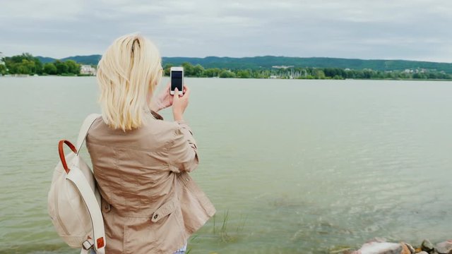 A woman takes pictures of a beautiful lake. Back view