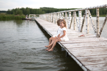Fototapeta na wymiar sisters Kicks feet on lake, childhood, light tone