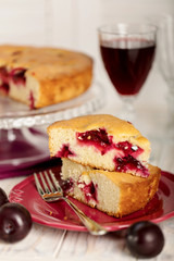 Homemade plum cake on a glass stand and red wine.