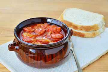 Vegetable stew with sliced sausage, lecho in ceramic pot with bread