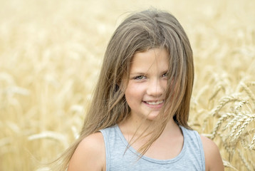 Head and shoulders portrait of adorable smiling little girl at a summer day with wheat field background