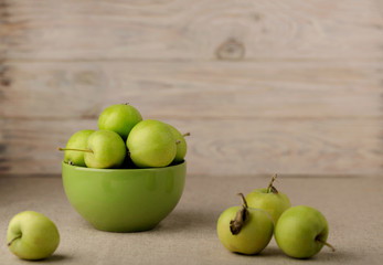 Green apples in a green plate on a wooden light background.