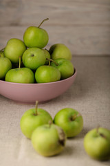Green apples in a lilac plate on a wooden light background.