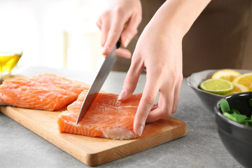 Woman cutting fresh salmon fillet on wooden board